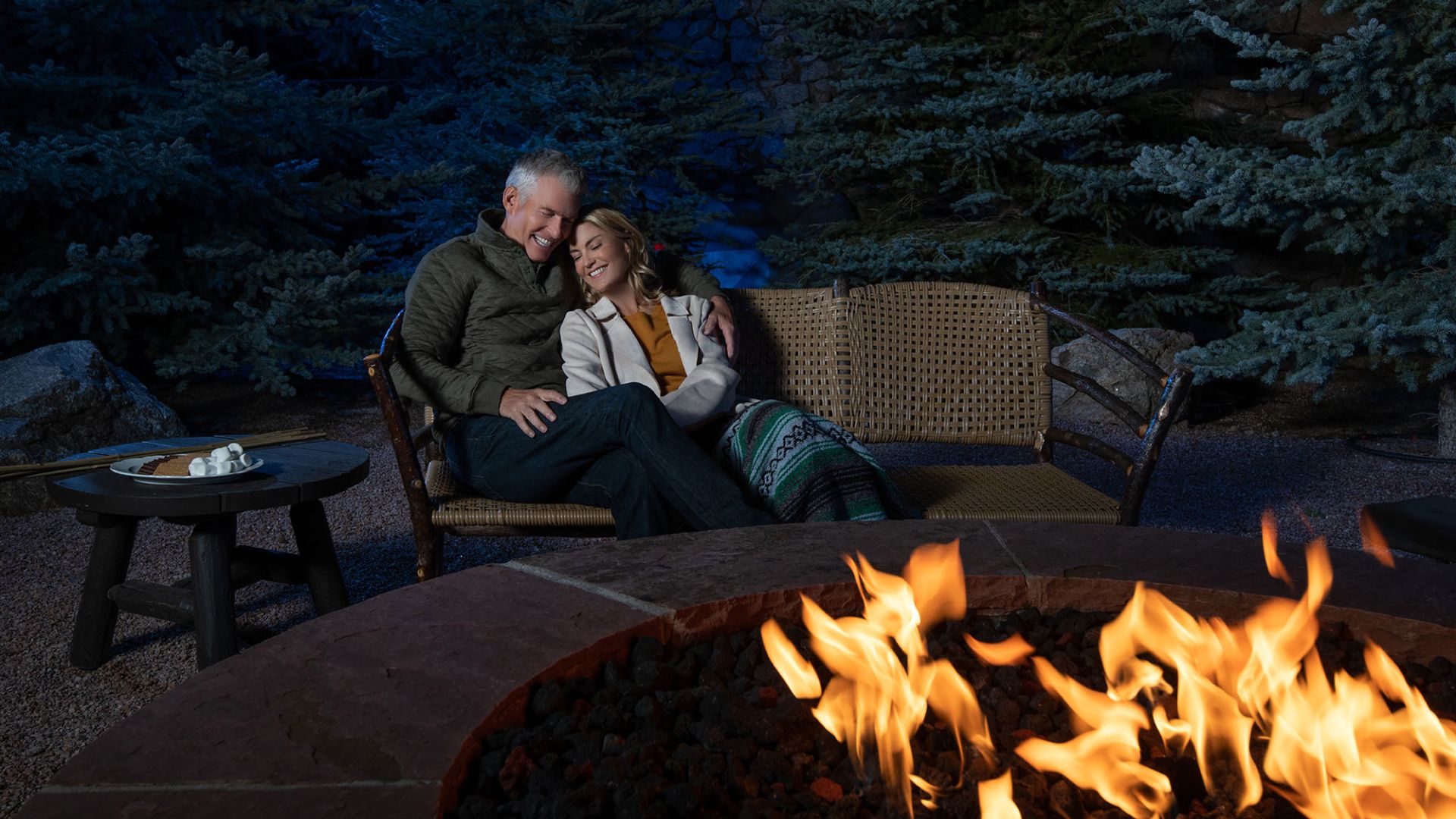 A Man And Woman Sitting On A Couch In Front Of A Fire